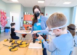 A young student drills into a board while being supervised by an adult.